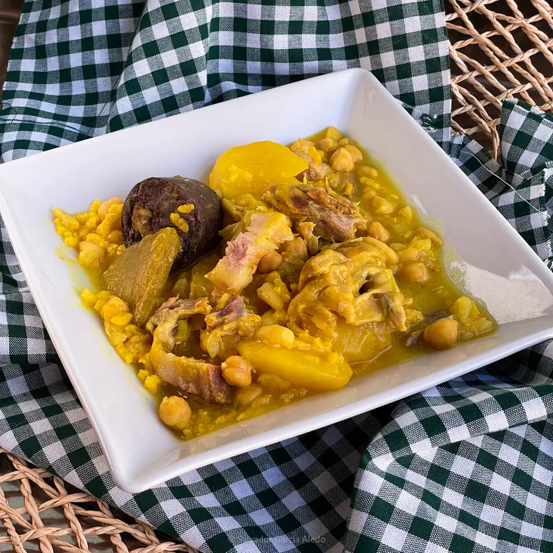 Cocido con garbanzos, patata, verdura y pelota en una fuente blanca sobre mantel de cuadros